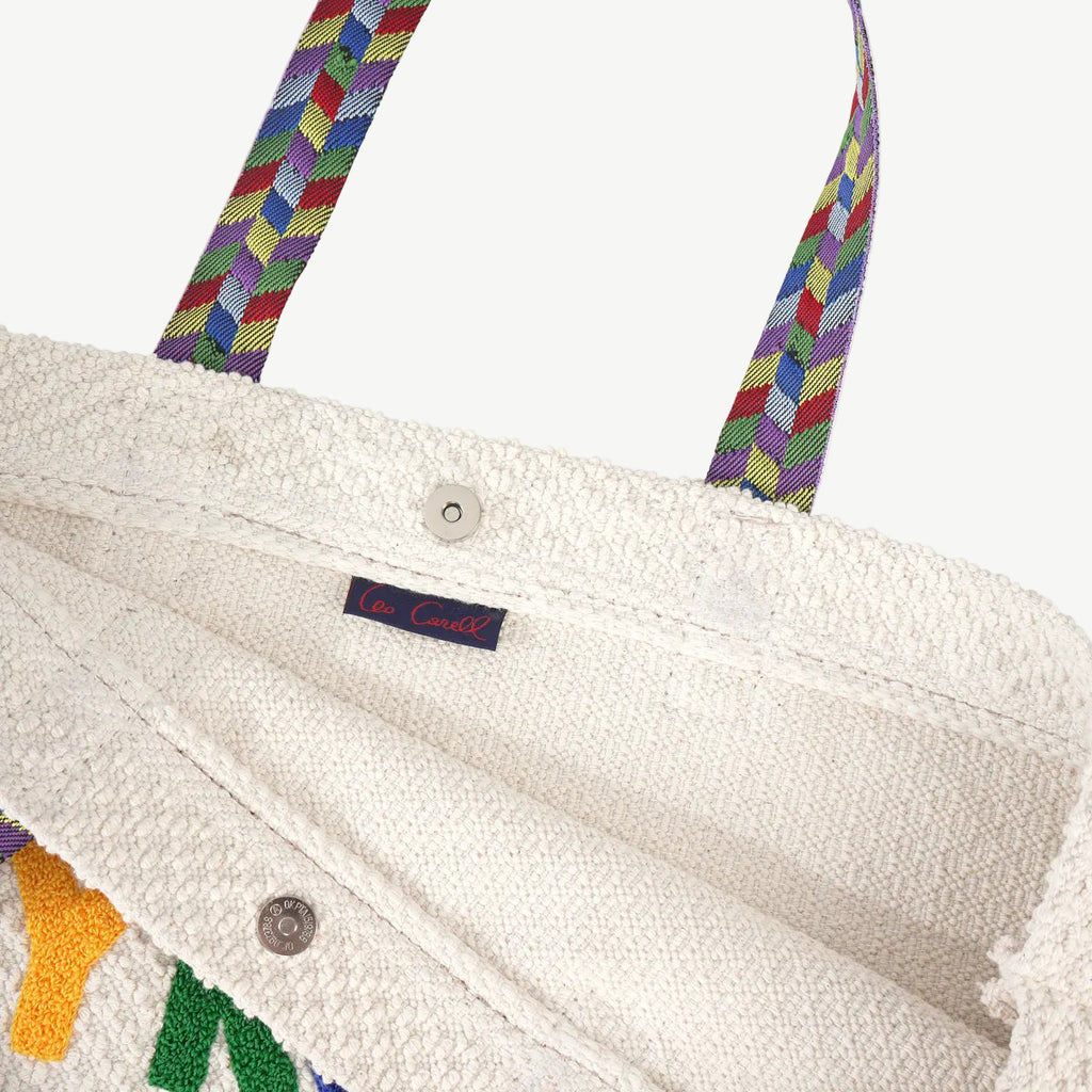 Close-up of a white textured bag with colorful handles and a visible brand label.